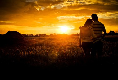 Zaljubljeni par gleda zagrljen prema zalasku sunca
