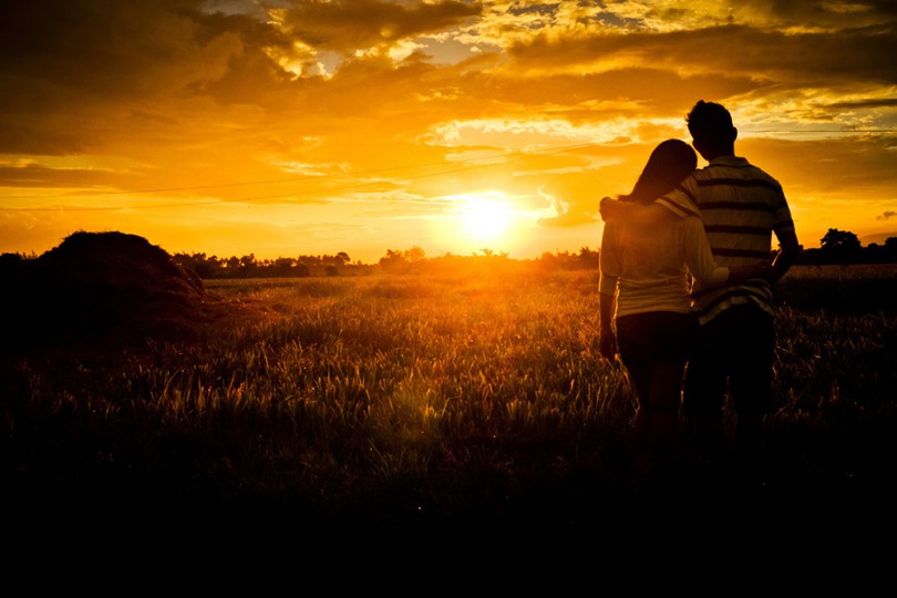 Zaljubljeni par gleda zagrljen prema zalasku sunca